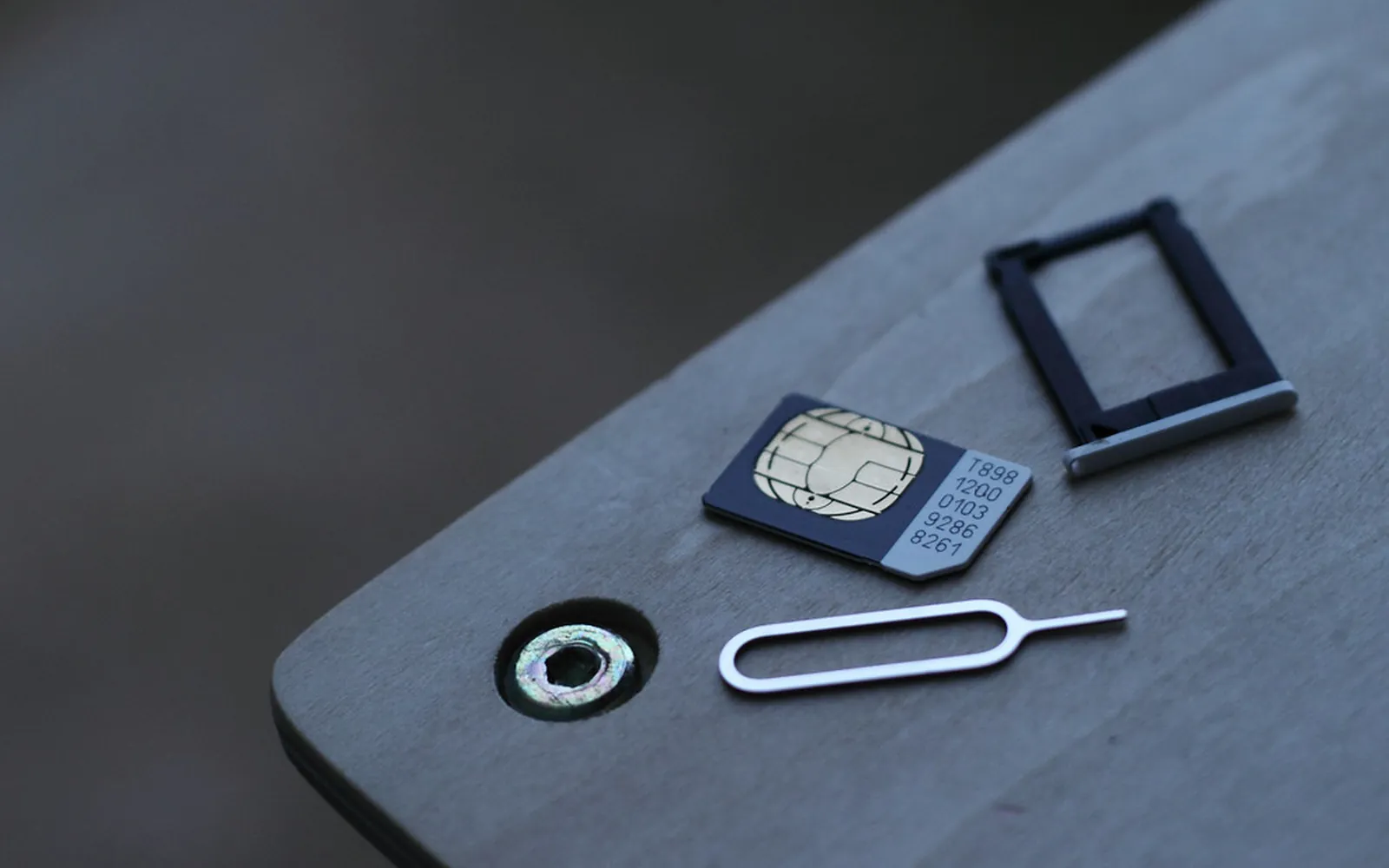 A nano SIM card, an empty SIM tray and a SIM ejector pin on a grey table